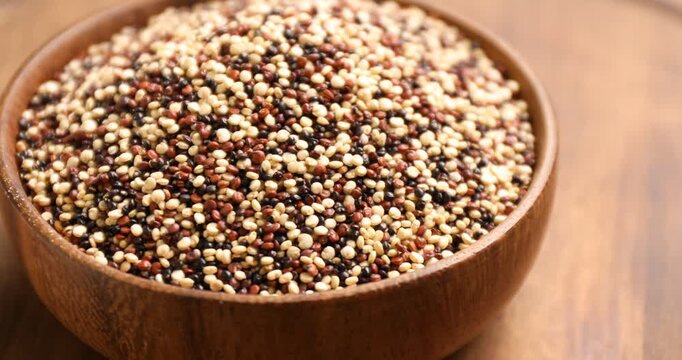 Raw mixed quinoa in bowl on wooden table, closeup