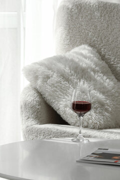 Glass of red wine on table near armchair in living room