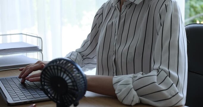 Woman working on laptop at desk with mini fan in office, closeup