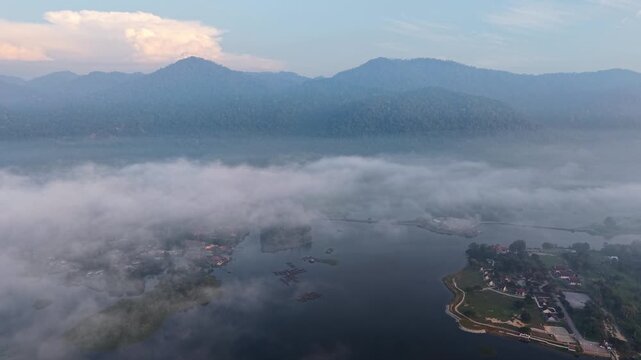 A serene aerial view of a river valley shrouded in mist with a mountain range in the background at Tasik Raban