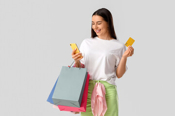 Happy young woman with mobile phone and credit card shopping online on white background