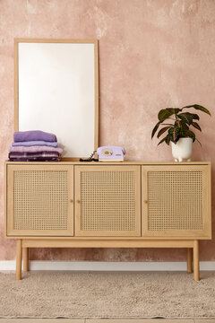 Stack of purple clothes with retro phone and houseplant on commode near grunge pink wall in room
