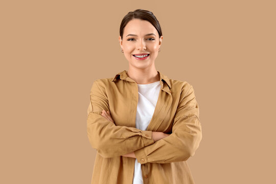 Young woman with dental braces smiling on beige background