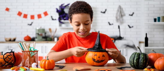 Naklejka premium Halloween celebration and childhood creativity, happy boy decorating a pumpkin with a witch hat for autumn holiday party in a decorated home kitchen
