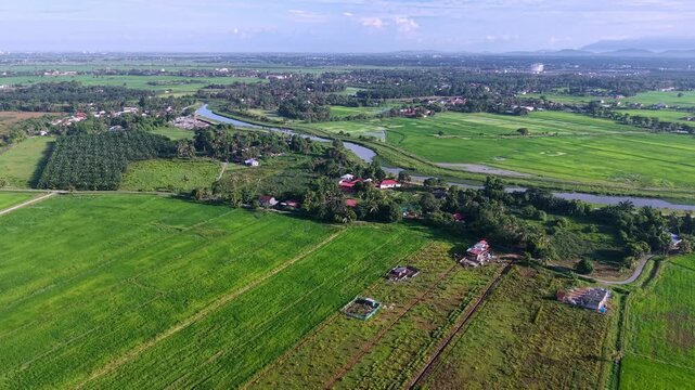 An aerial shot showcasing expansive farmland with vibrant green fields, waterways, and scattered farmhouses in a peaceful rural landscape at Kubang Semang