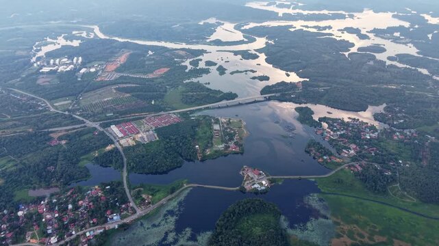 Aerial shot of a serene rural landscape featuring a river, bridge, small houses, dense forest at Tasik Raban