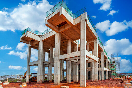 Massive reinforced concrete pillars and framework at a construction site against a blue sky, featuring heavy machinery and scaffolding on the dirt ground.