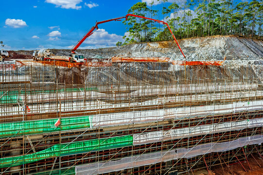 Concrete pump truck pouring cement over a massive steel rebar foundation at a large industrial construction site.