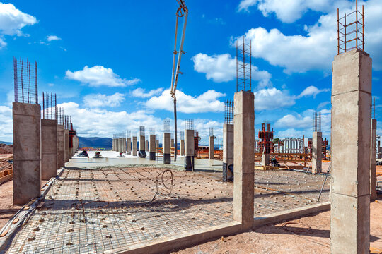 Construction site with concrete columns and rebar mesh foundation under a blue sky with white clouds, architectural structure development.