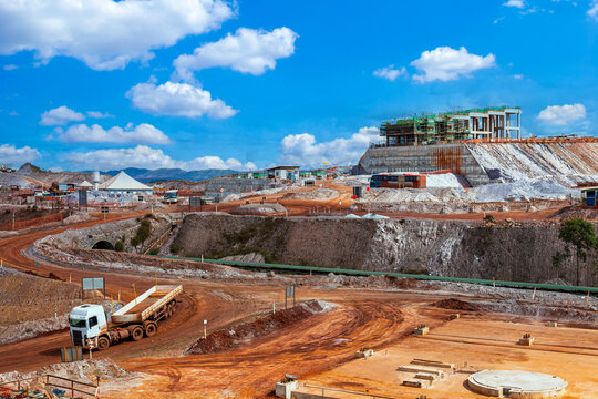 Large-scale infrastructure construction for an iron ore mine in Brazil, featuring heavy transport trucks, earthworks, and concrete structures under a blue sky.