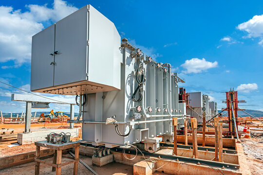 Large industrial electrical transformers installed at a construction site under a bright blue sky, highlighting power grid infrastructure and energy development.