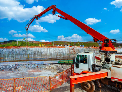 Large-scale construction site featuring a concrete pump truck working over reinforced steel foundations and safety fences under a bright blue sky.