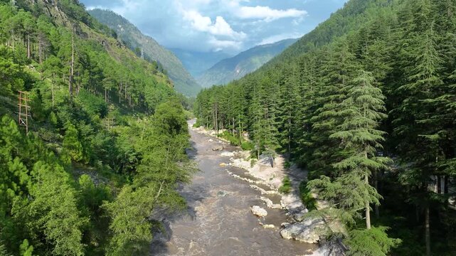 Drone pullback reveal of the winding mountain river carving through steep forested Himalayan slopes on the scenic route to Kasol in Kullu District.