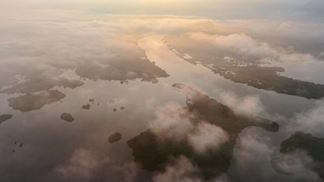 Aerial perspective captures a river flowing through clouds. Sunlight glints on the water's surface at Tasik Raban