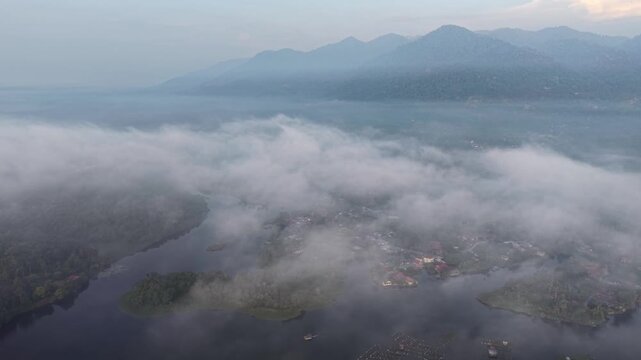 Aerial view captures misty mountains and a winding river. Soft clouds drift over valleys and hills at Tasik Raban