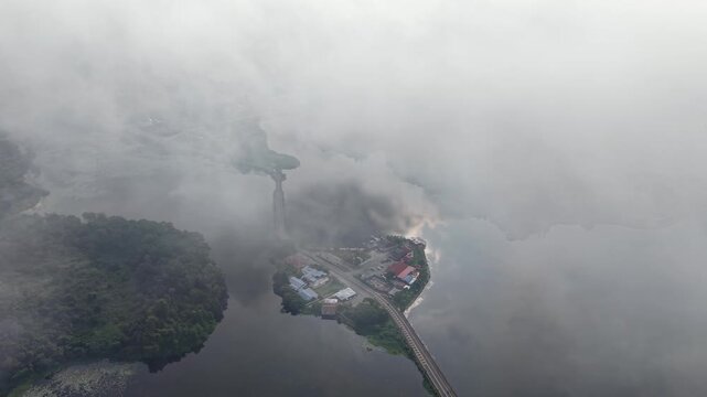 Aerial shot shows a fog shrouded island. Thick clouds wrap the landscape at Tasik Raban