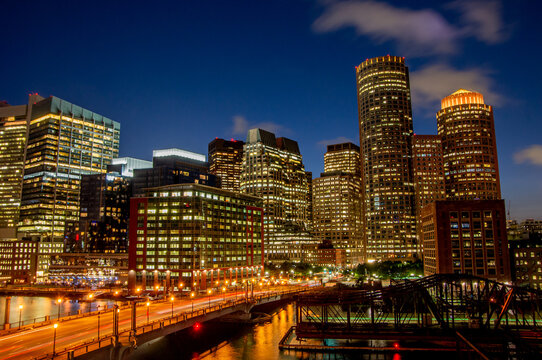 Boston, MA &mdash; Aug. 20, 2018: Downtown towers glow at dusk beyond Fort Point Channel, with traffic light trails and the historic Northern Avenue Bridge in the foreground.