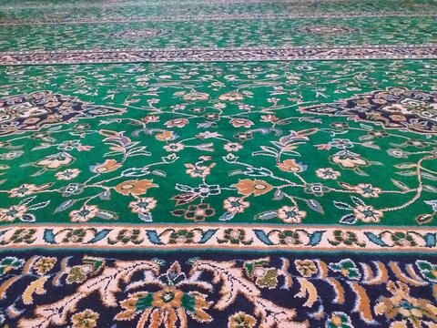 Green prayer carpet with intricate floral patterns woven into detailed textile rug, suitable for interior design projects and religious themed designs.