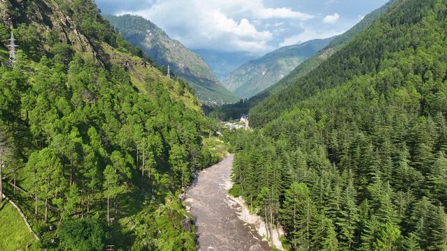 Wide drone establishing shot over the Parvati River basin surrounded by towering green mountain peaks near Kasol in Kullu District, India.