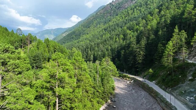 Wide drone establishing shot over the Parvati River basin surrounded by towering green mountain peaks near Kasol in Kullu District, India.