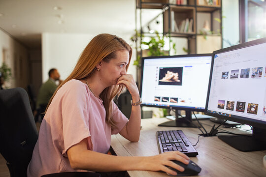 Young woman editing photos on dual monitors in modern office