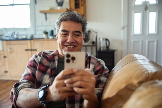 Smiling man using smartphone on couch at home