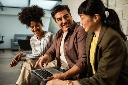 Diverse coworkers collaborating on laptop in modern office