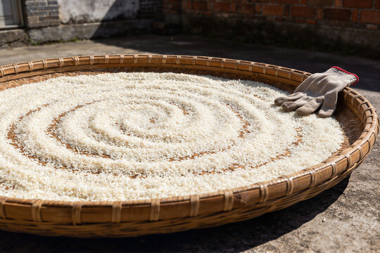 Woven bamboo winnowing tray filled with white rice drying in a sunny courtyard