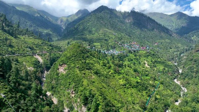 Aerial shot over the colorful tin roofs and lush agricultural terraces of Barshaini village, a vibrant trekking basecamp in the Parvati Valley of Himachal Pradesh, India.