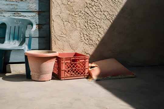 Old Patio Chair Pot Crate and Worn Cushion Against Weathered Wall