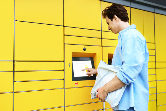 man uses a yellow parcel locker terminal for a contactless delivery pickup. This self-service logistics technology simplifies ecommerce online shopping and shipping.