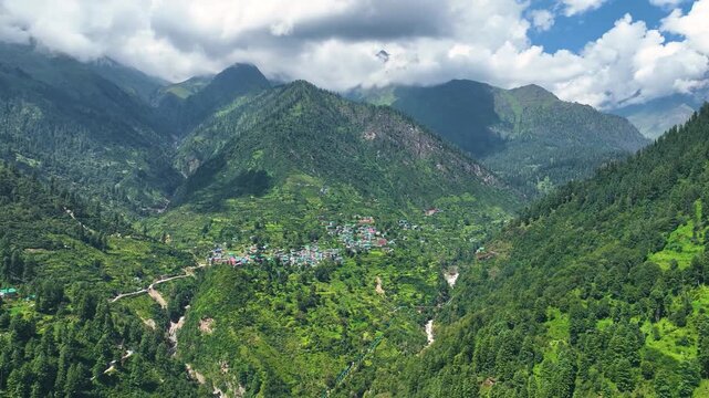 Aerial shot over the colorful tin roofs and lush agricultural terraces of Barshaini village, a vibrant trekking basecamp in the Parvati Valley of Himachal Pradesh, India.