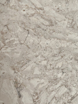 A high-resolution photograph of natural, broken stone pieces forming a complex brecciated marble texture. The image shows fractured patterns in cream, beige, and light grey