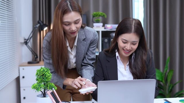 Two business women are sitting and talking in the office and discussing projects on laptops and graphs working together in the office.