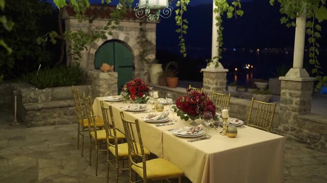 Night wedding dinner table on stone terrace with gold chairs and red roses