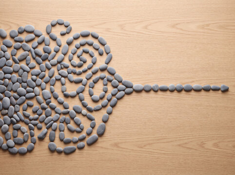 Pebbles arranged on a light wooden background form an intricate brain pattern.