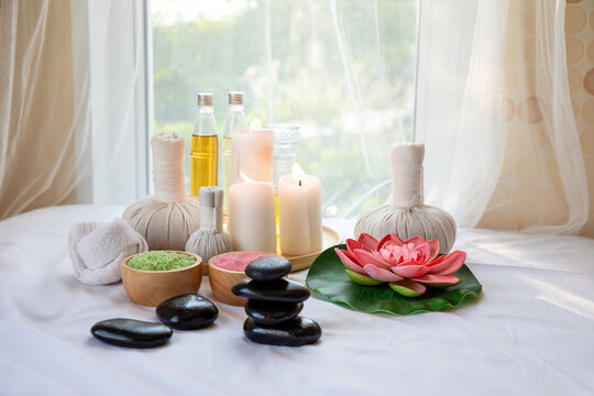 Spa wellness arrangement with herbal compress balls, candles, massage oil, bath salt, black stones and lotus flower for relaxation, therapy, beauty and body care