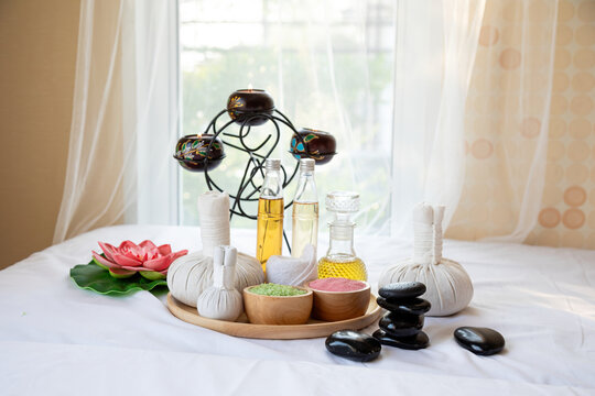 Spa massage therapy arrangement with herbal compress balls, essential oil, bath salt, hot stones, candle and lotus flower for wellness relaxation