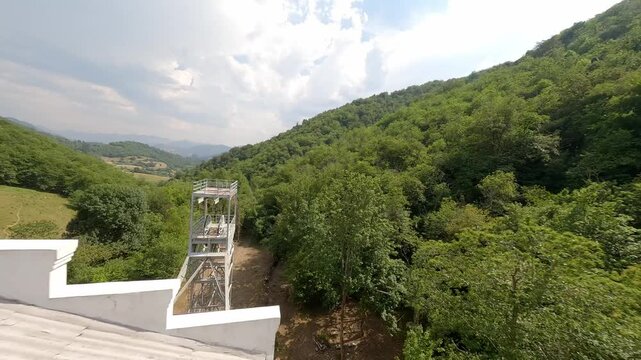 Aerial view of the historic Pozo de San Fernando mining structure surrounded by dense green forests in Aller, Asturias, Spain. Suitable for industrial heritage and sustainability documentaries.