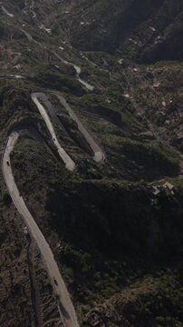Aerial drone shot flying over a serpentine road with cars driving through the rugged, arid mountains of taiz, yemen, revealing remote villages nestled among the green and brown landscape. In taiz yeme