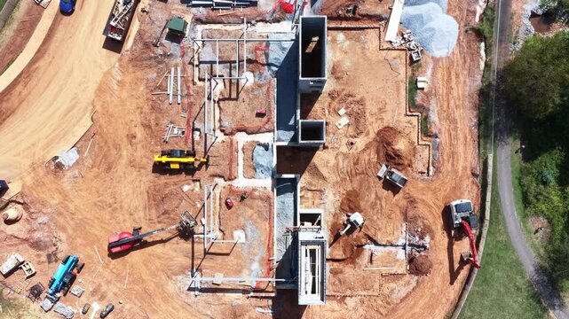 Fresh footings and plumbing runs mark out a building pad in Lynchburg, Virginia, excavators and lifts parked across the graded red clay around the slab. Aerial top down flyover