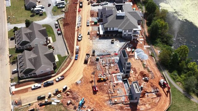 An apartment complex rises beside a green pond in Lynchburg, Virginia, red clay graded around new foundations while finished buildings stand along the drive. Aerial view