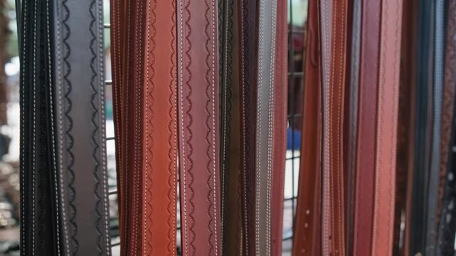 Rows of handcrafted leather belts hang neatly from a vendor display at an outdoor flea market in Colorado