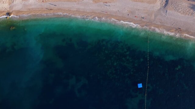 Aerial view of sandy beach and clear blue sea at sunset, showing shoreline detail