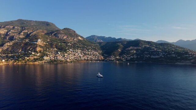 Aerial view of Montecarlo coastline with yacht on calm sea at sunset, mountains behind