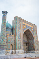 Detailed exterior view of Sher-Dor Madrasa at Registan Square in Samarkand, Uzbekistan, featuring a turquoise dome, tall minaret, monumental pointed portal, intricate geometric mosaics © pploylp