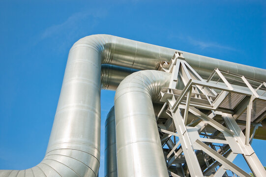 The photo shows a close-up of a straight pipeline on a metal support against a blue sky