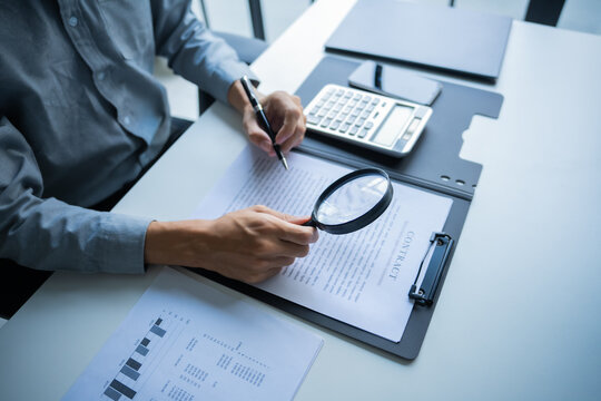Asian businessman holding magnifying glass and pen checking documents on working table