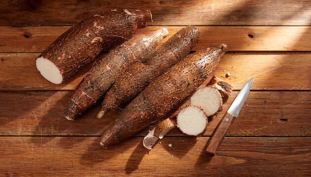 Fresh Raw Cassava Roots with Knife on Rustic Wooden Table for Traditional Cooking Preparation
