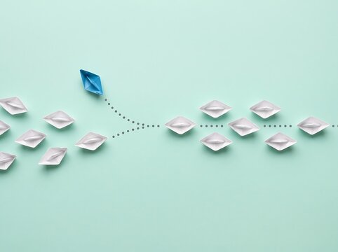 Blue paper boat changing direction from group of white boats